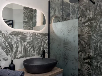 Bagno moderno con lavabo in pietra nera, specchio retroilluminato e piastrelle a foglie tropicali