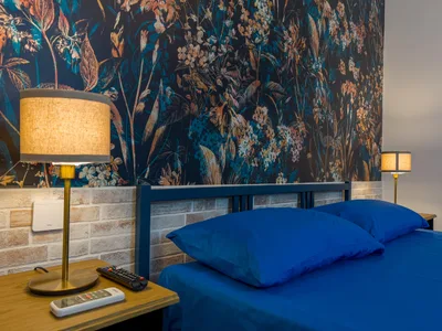 Camera matrimoniale con letto blu, testiera in legno, carta da parati floreale scura e lampade da comodino (foto di copertina)