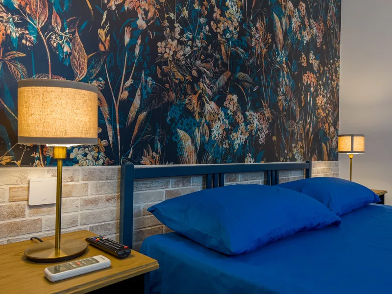 Camera matrimoniale con letto blu, testiera in legno, carta da parati floreale scura e lampade da comodino (foto di copertina)