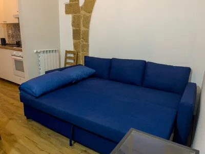 Divano letto matrimoniale aperto nel soggiorno, con colonna in pietra e angolo cucina sullo sfondo