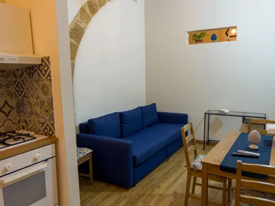 Soggiorno con divano blu sotto l'arco in pietra, zona pranzo e angolo cucina con piano cottura